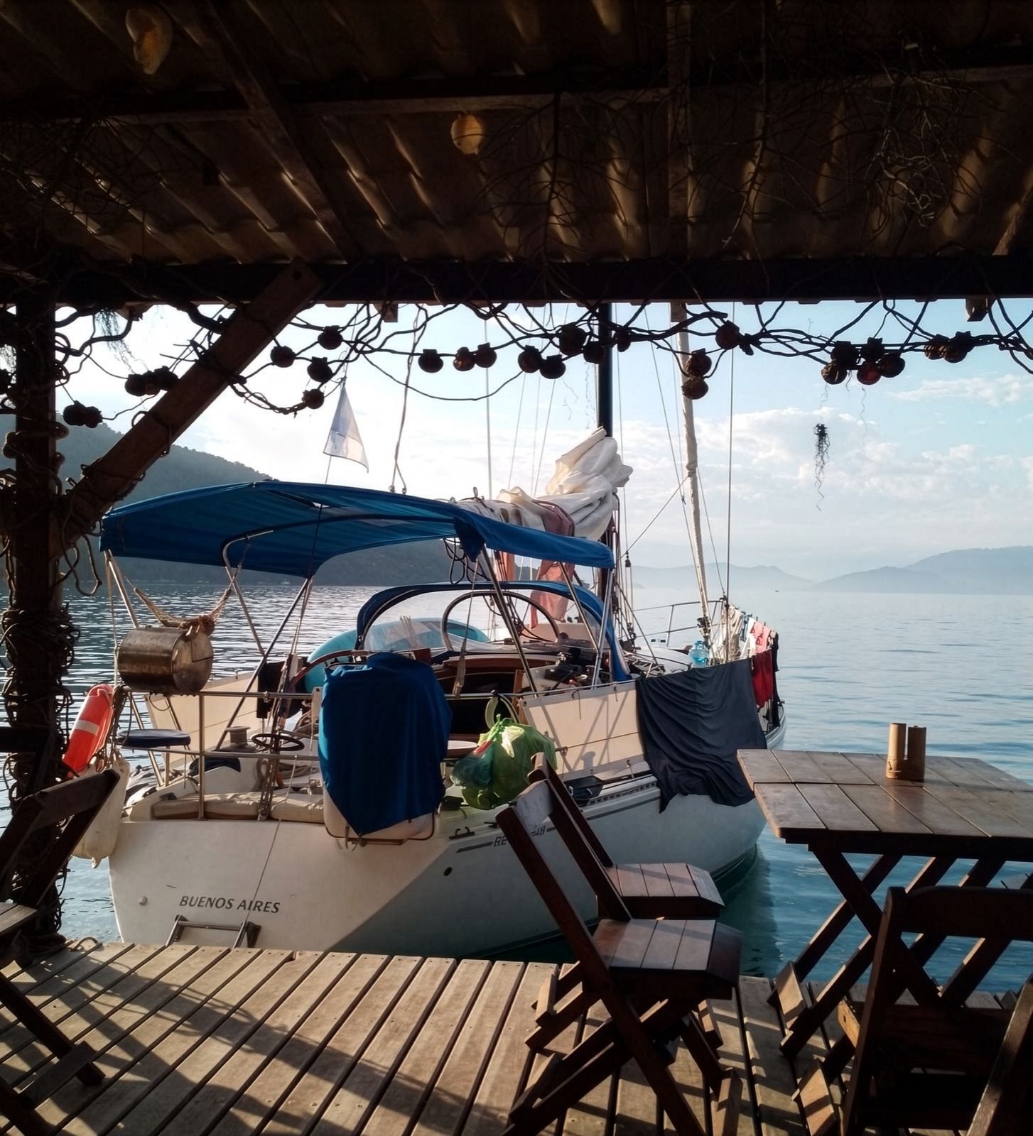 El velero amarrado junto a un muelle de madera, con las sierras al fondo
