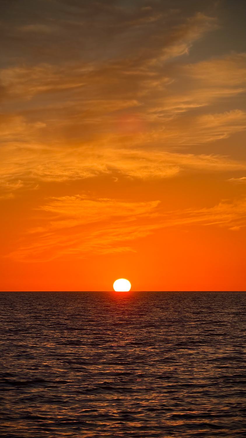 El sol metiéndose en el horizonte, mar abierto y cielo anaranjado