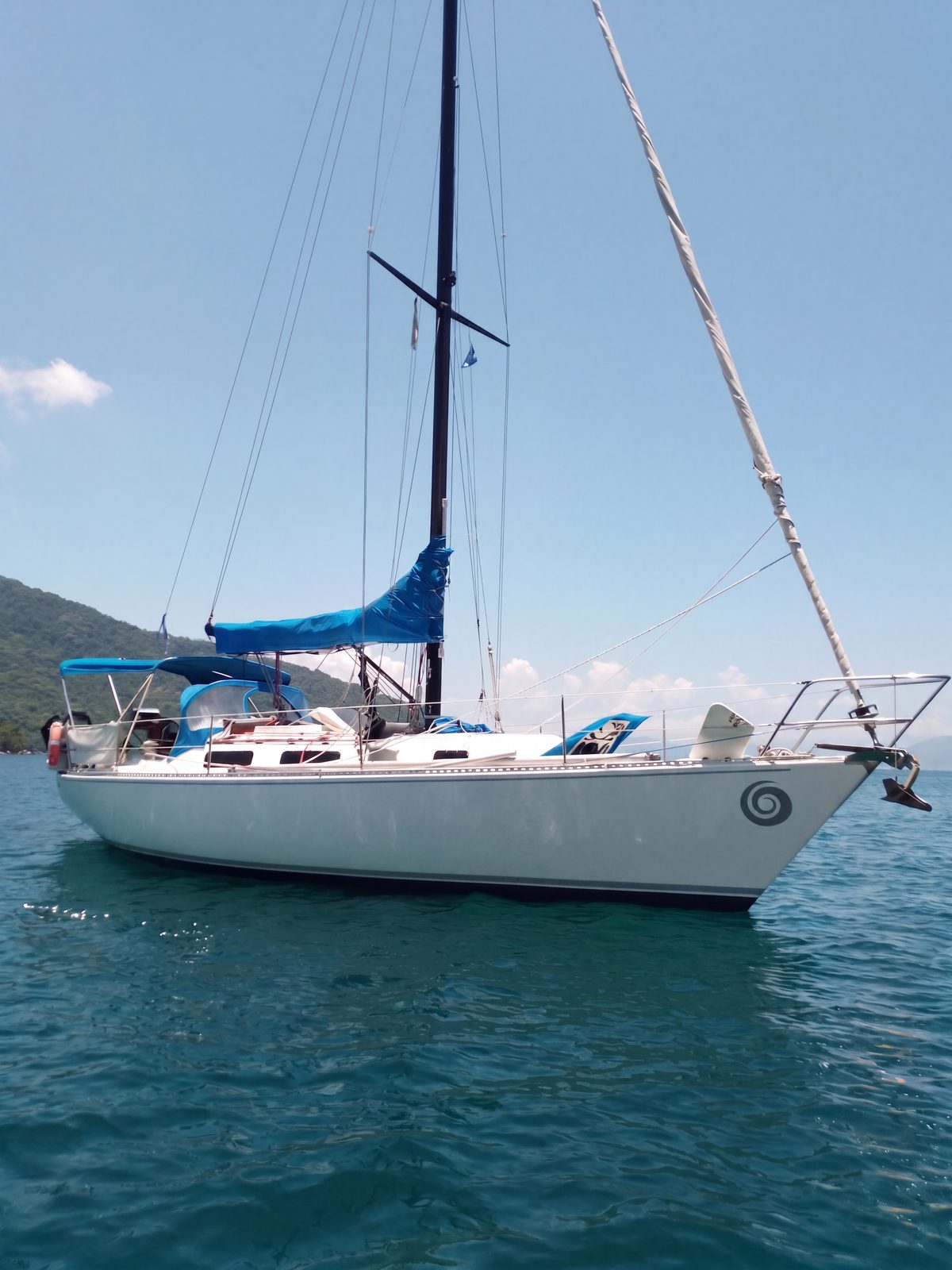 El velero fondeado de perfil, con la costa arbolada al fondo